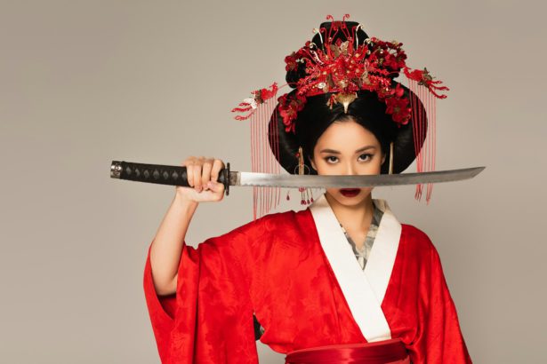 Japanese woman holding sword near face isolated on grey