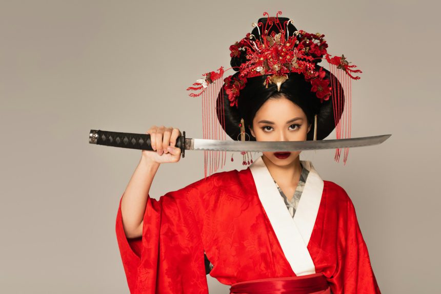 Japanese woman holding sword near face isolated on grey