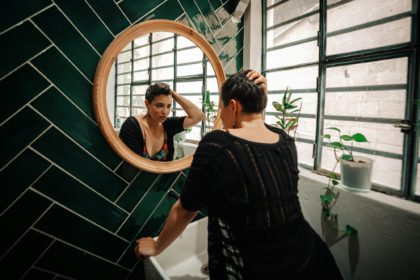 Young Middle Eastern short-haired woman looking at herself in the mirror in the bathroom.