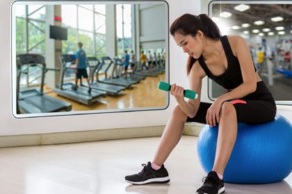 Young woman preparing and sitting on a ball reflect with glass before exercise in the fitness room