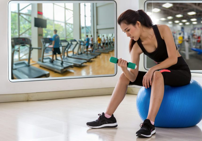 Young woman preparing and sitting on a ball reflect with glass before exercise in the fitness room